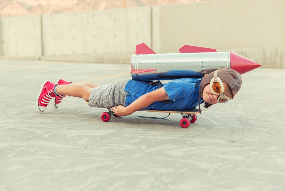 Kid lying on a skateboard with a rocket on his back.. looks really fast